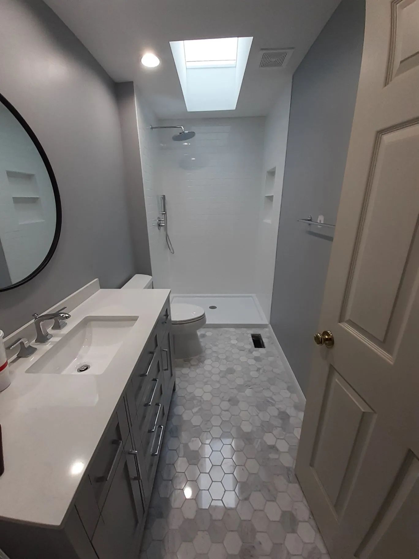 Bathroom with a gray vanity, walk-in shower, skylight, and hexagonal floor tile