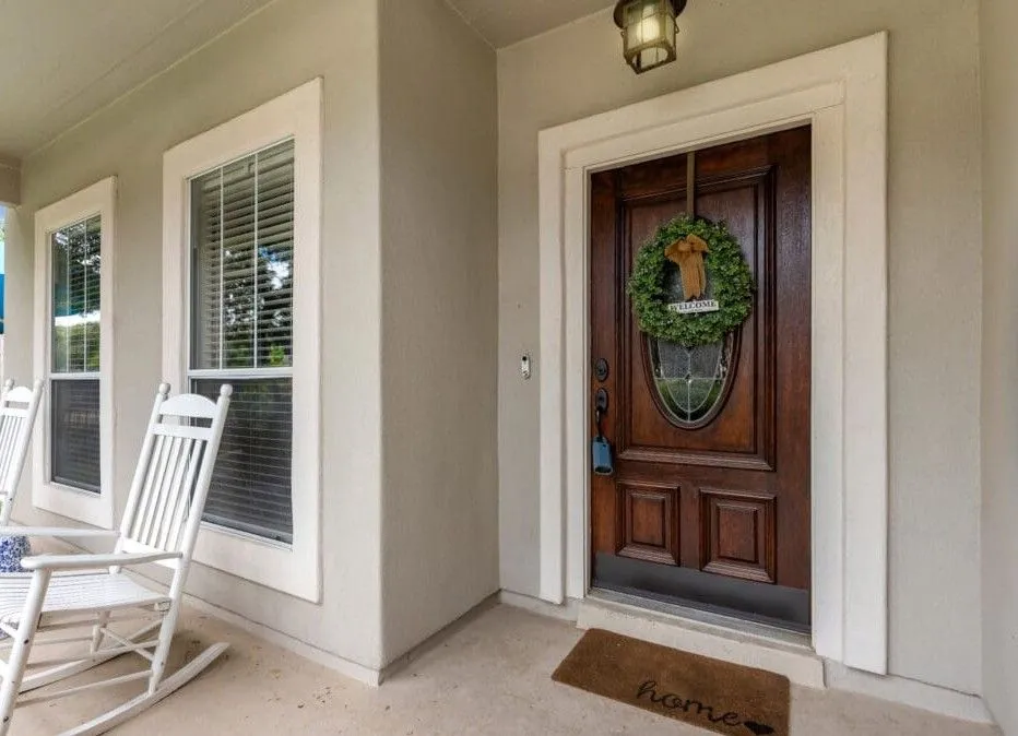 Covered front porch with white rocking chairs, windows, and a dark wood entry door decorated with a wreath